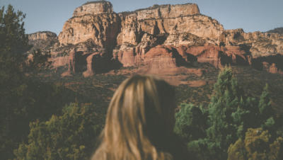 Desert mountains in the background with trees below, as seen from the perspective of female onlooker, marked by the back of her head